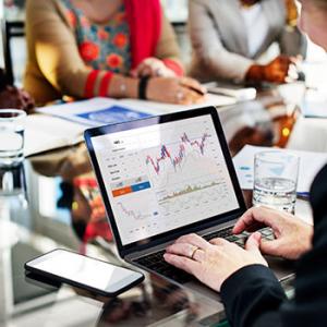 Central bancaria y de representación - Persona con traje negro trabajando frente a su portátil en una sala de reuniones con su móvil